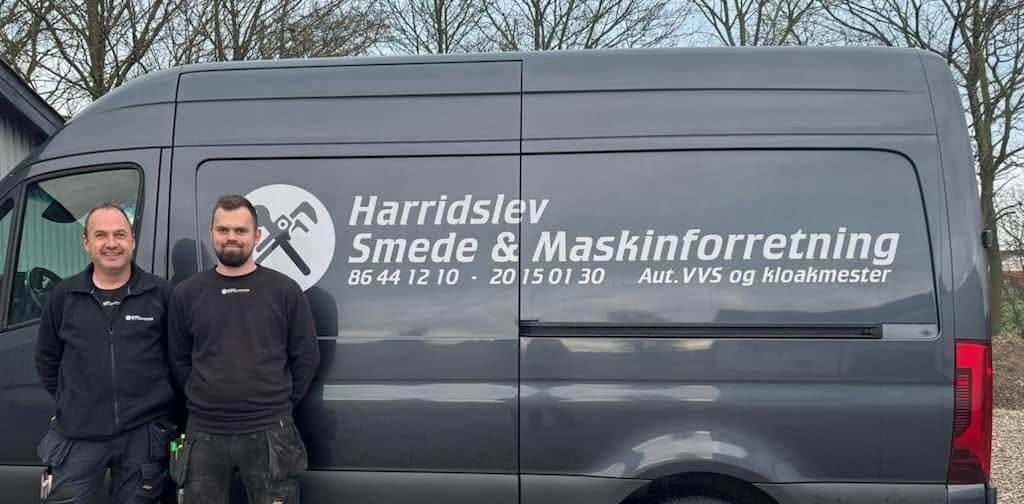 To personer står ved siden af en varevogn med teksten "Harridslev Smede & Maskinforretning" på siden.