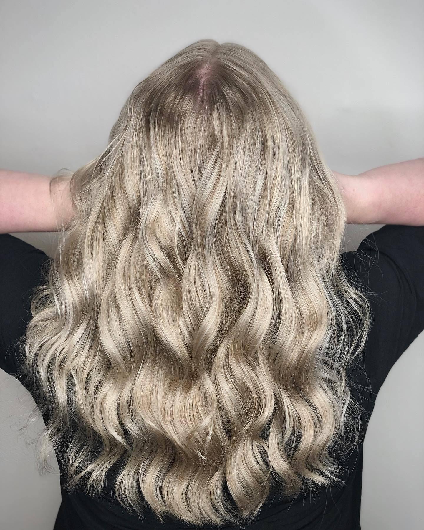 Langt, bølget hår i lys blond farve, set bagfra med hænderne løftet op.