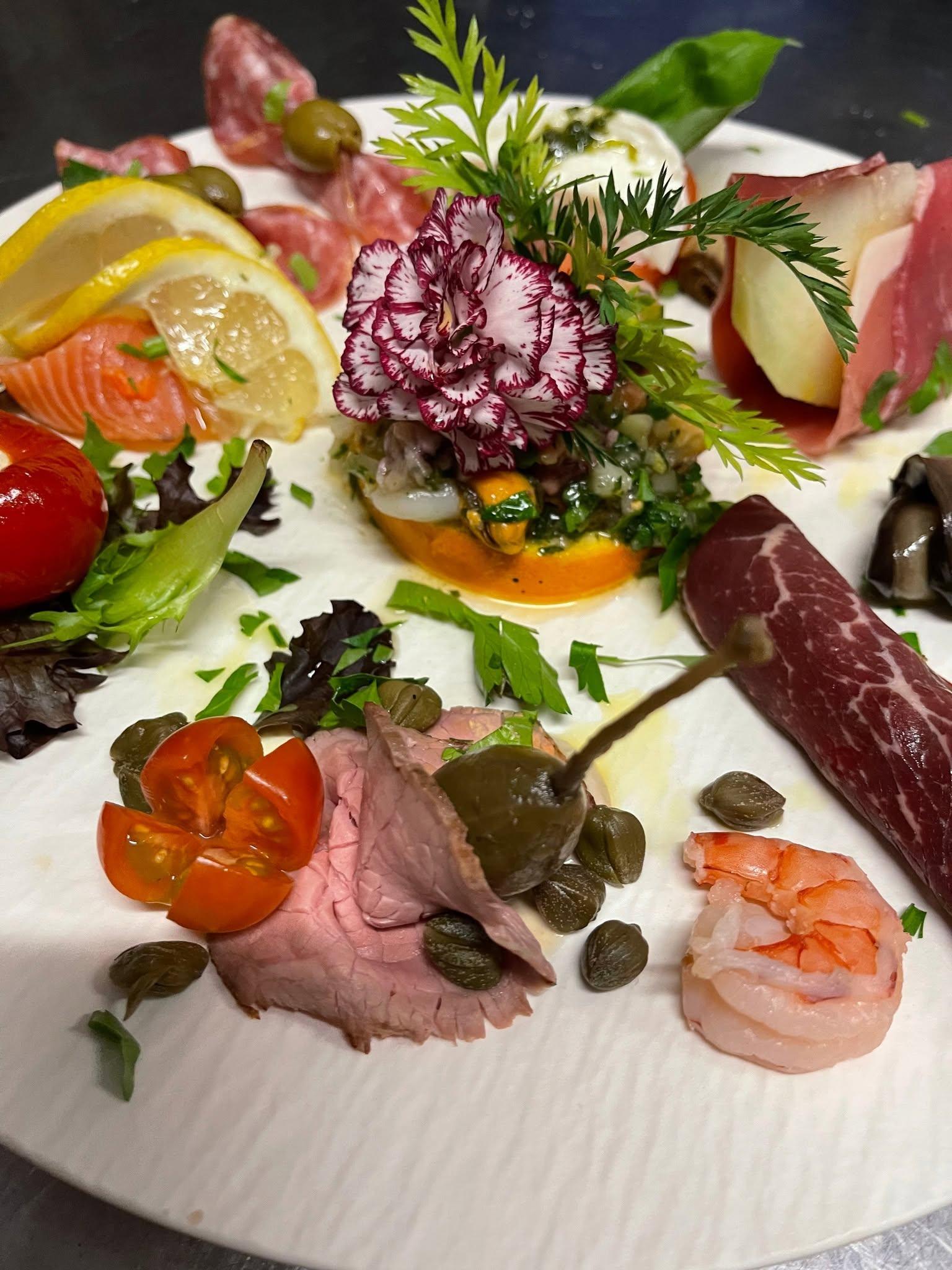 En farverig tallerken med forskellige delikatesser, herunder skaldyr, kød, grøntsager og friske urter.