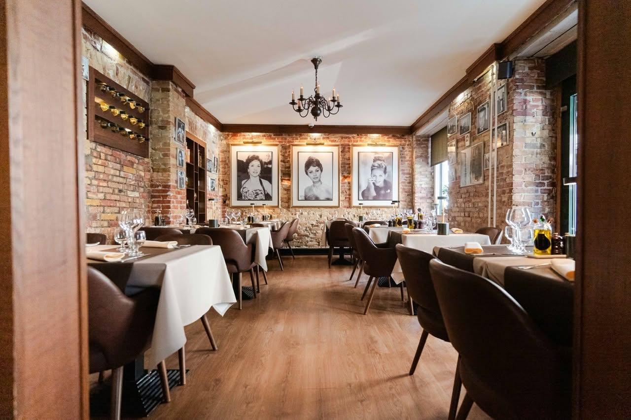 En elegant restaurant med trævægge, borddækning og portrætter af kvinder på væggene.
