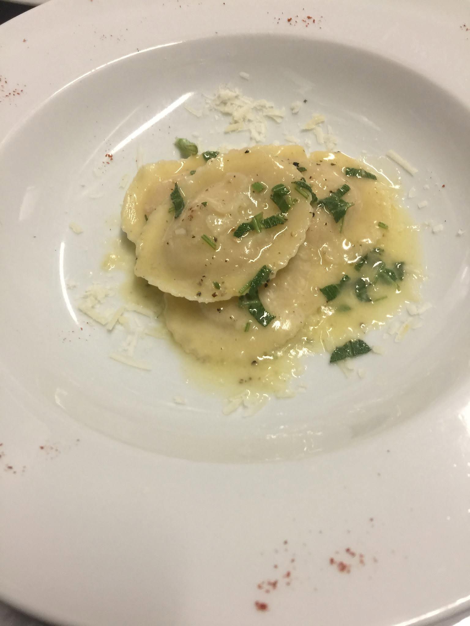 Ravioli med smør og friske krydderurter på en hvid tallerken.