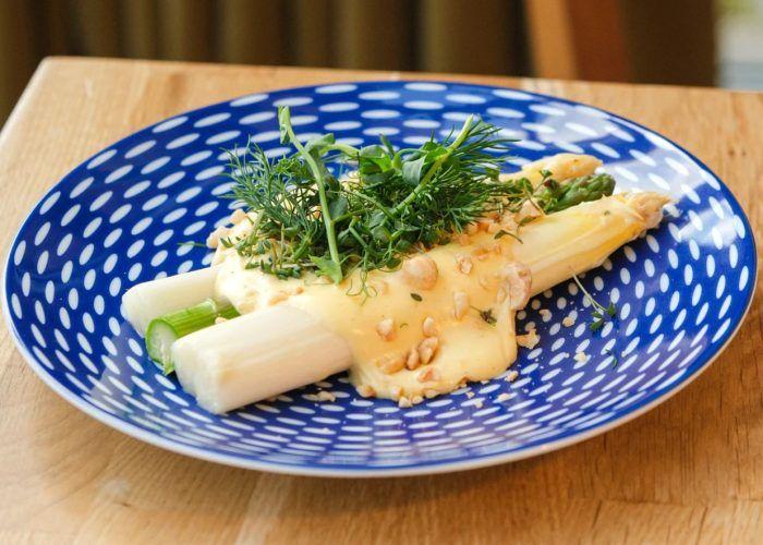 Lækre asparges med hollandaise sauce og friske krydderurter på en blå tallerken med prikker.