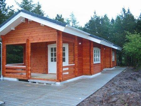 Et moderne træhus med en stor veranda, omgivet af skov og natur.