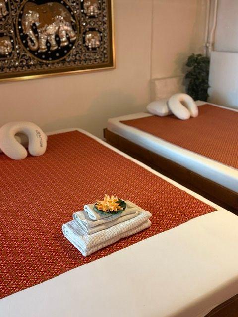 To værelser med massageborde, dekoreret med håndklæder og en blomst i en skål på bordet.