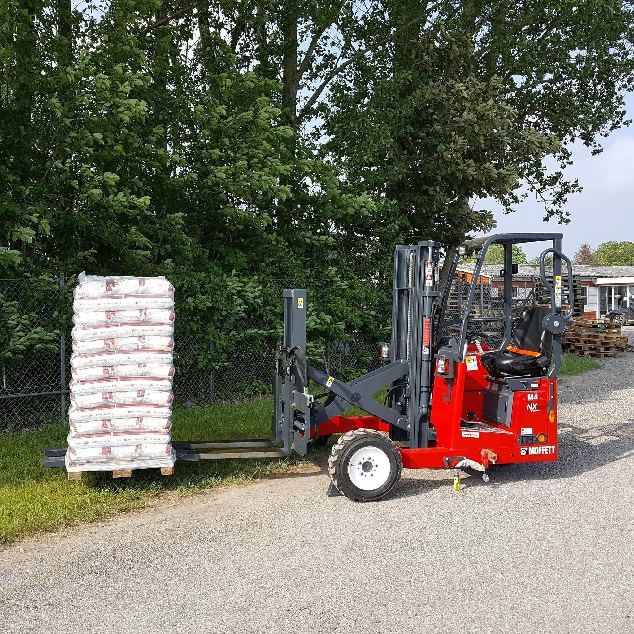 En rød gaffeltruck står ved siden af en stak med sække på en palle langs en grusvej.