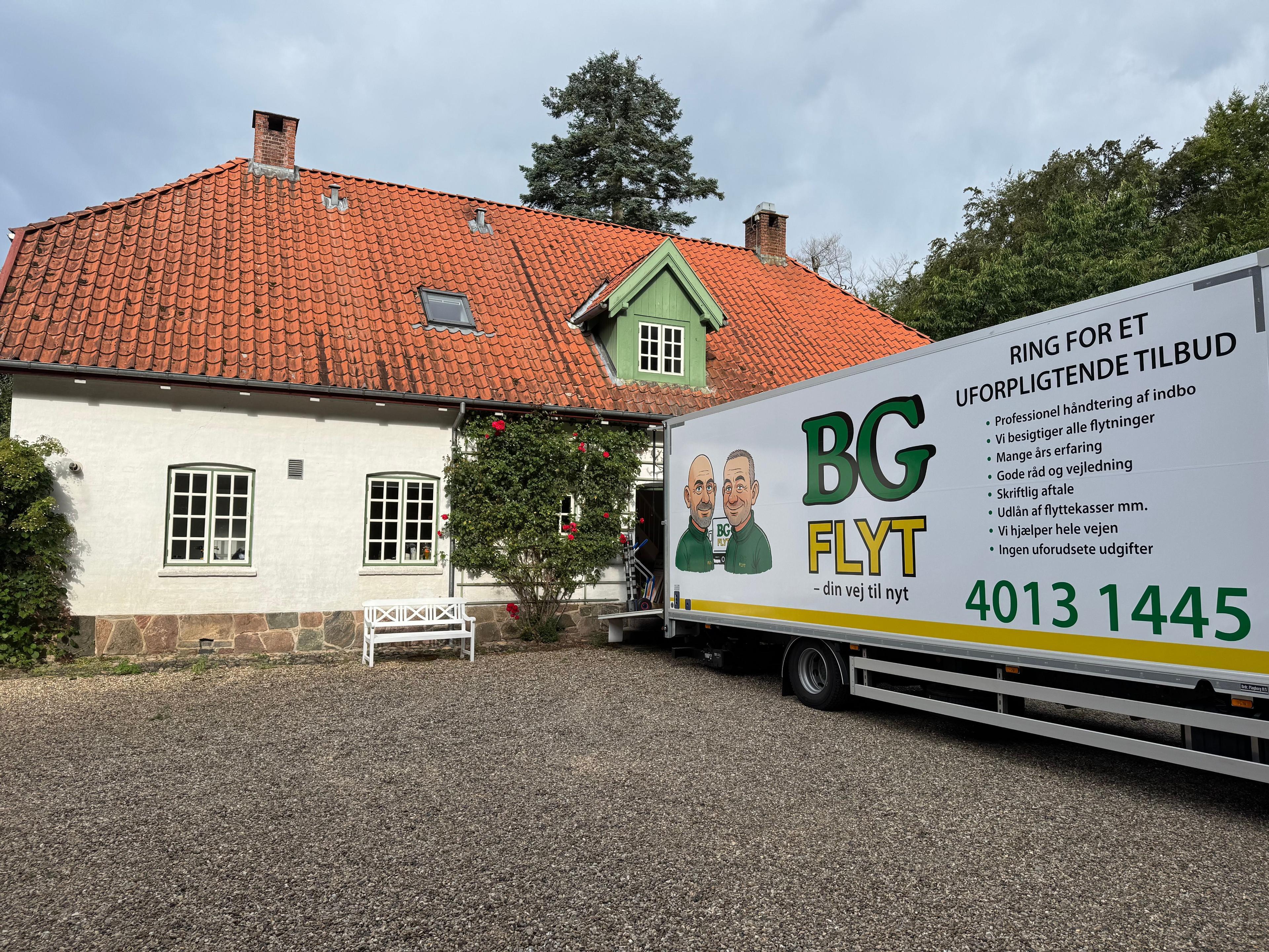 Hus med rød tag og grønne detaljer, parkeret flyttebil fra BG FLYT i indkørslen.