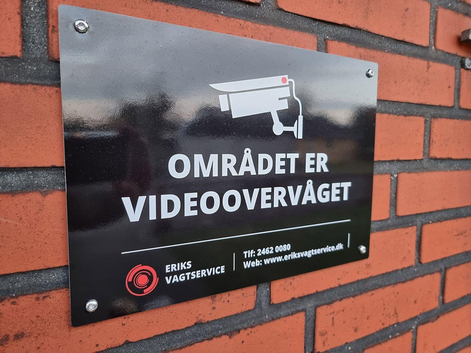 Skilt der advarer om videoovervågning i området, monteret på en murstensvæg.