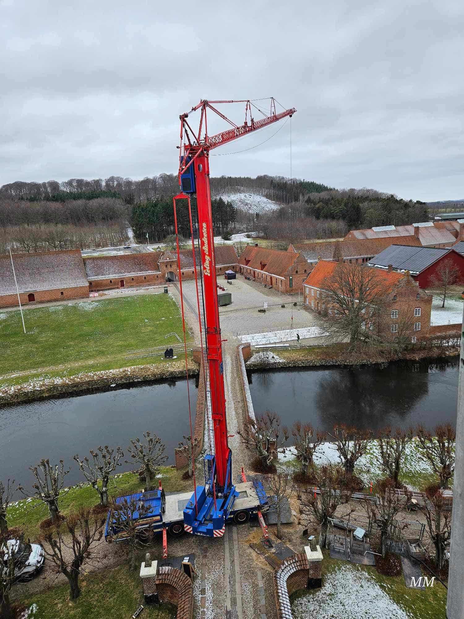 Kran står på en byggeplads ved en kanal, omgivet af bygninger og træer i vintervejr.