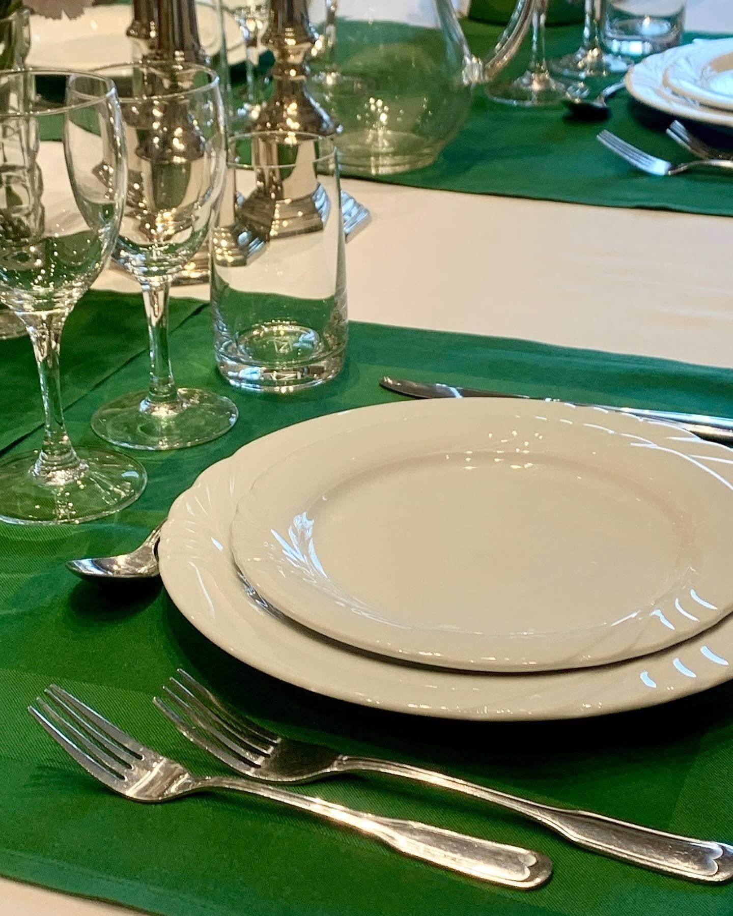 Dækning af et bord med hvidt porcelæn, glas og bestik på en grøn dug.