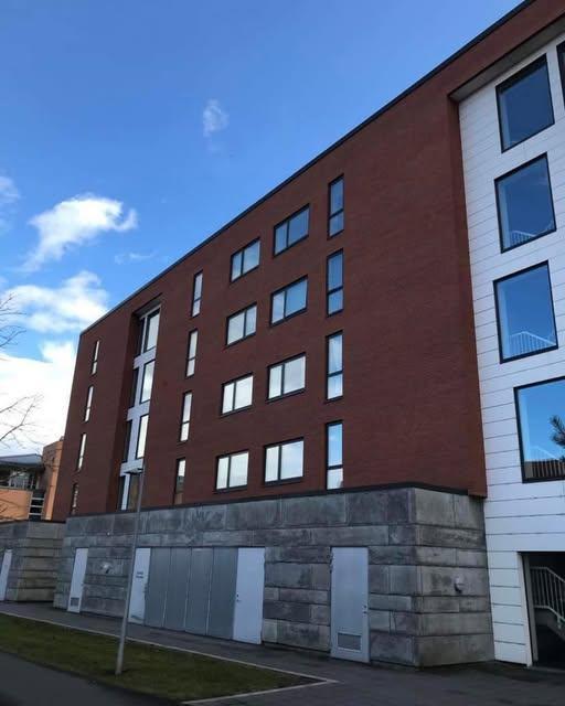 Moderne bygning med røde mursten og store vinduer under en blå himmel.