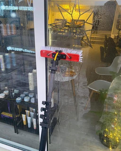 Rengøringsredskab med børste ved et vindue, der viser en restaurant med stole og borde i baggrunden.