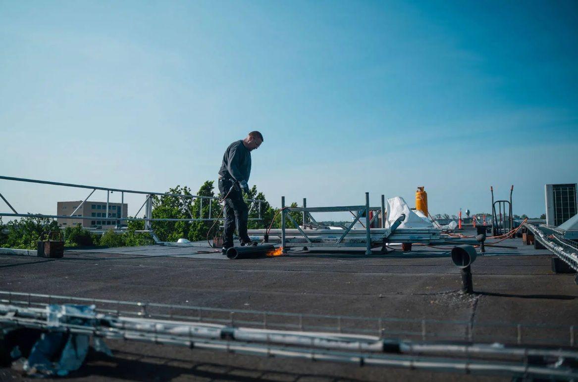 En håndværker arbejder på et tag med solpaneler under en klar blå himmel.