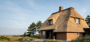 Et charmerende hus med stråtag beliggende i et naturskønt område med træer og udsigt over landskabet.