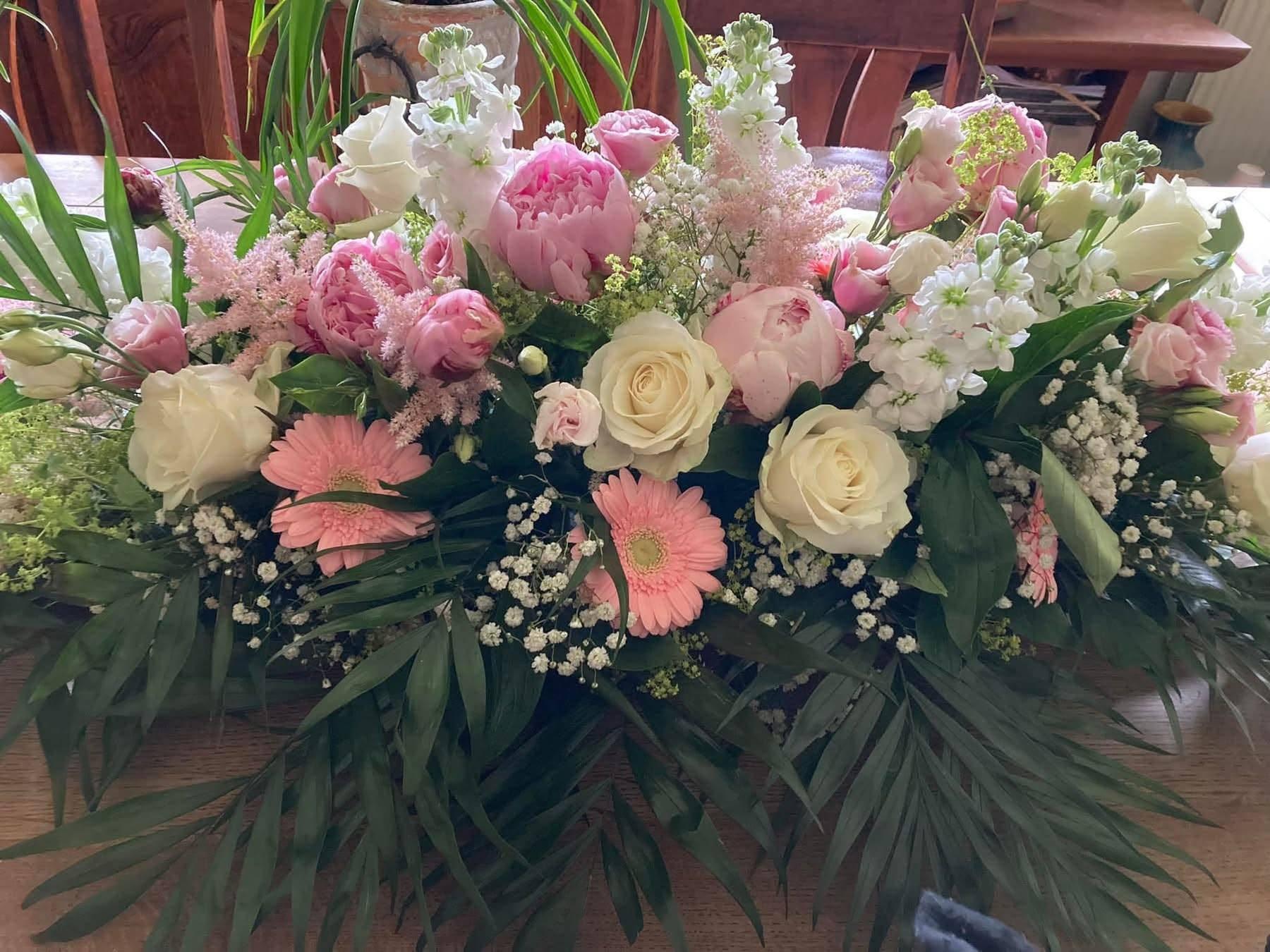 En smuk blomsterdekoration med lyserøde og hvide roser, pæoner, gerberaer og grønne blade.