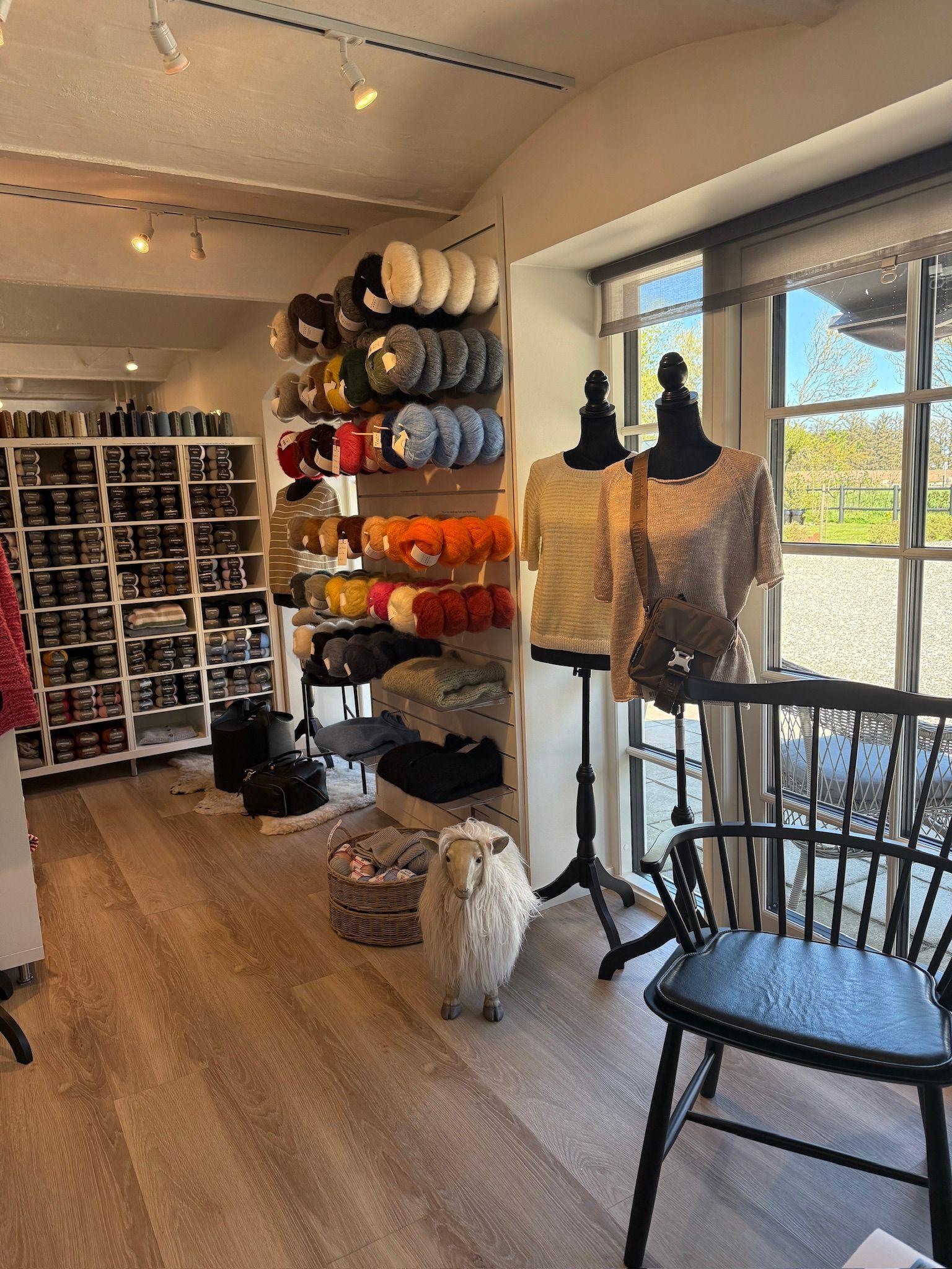 Inde i en butik med garn, hvor der er garnnøgler på hylder og en stol ved vinduet.