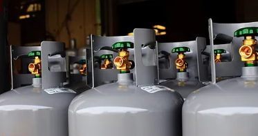 Gasflasker med grønne ventiler og gyldne tilslutninger i en lagerhal.