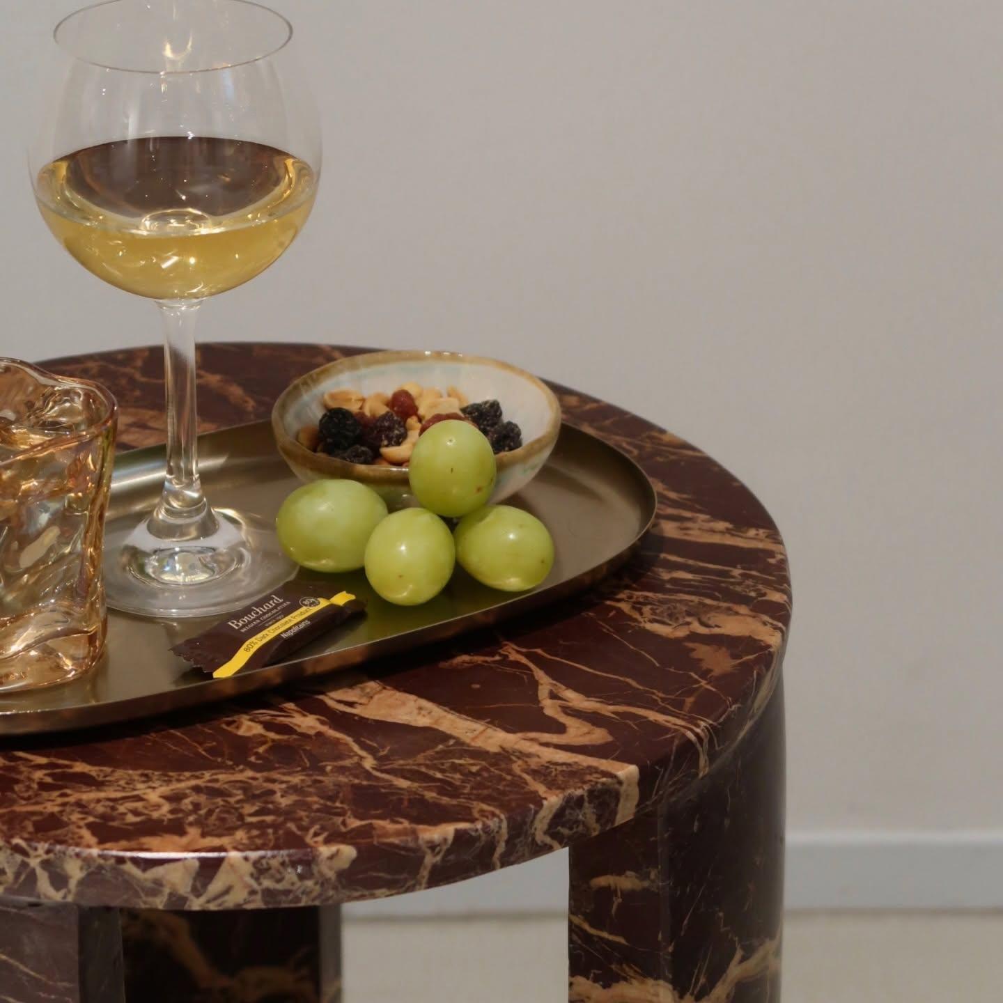 Et marmorbord med et glas hvidvin, en skål med nødder og druer samt en chokoladebar på en bakke.