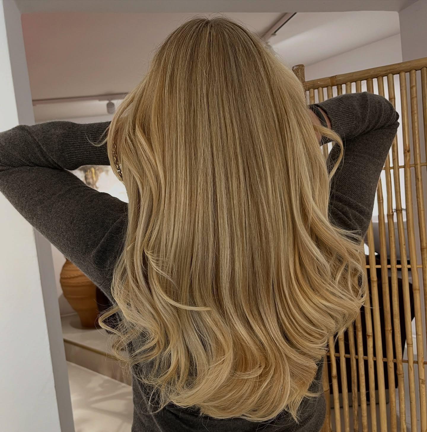 Langt, bølget hår i lys blond farve, set bagfra, med hænderne løftet over hovedet.