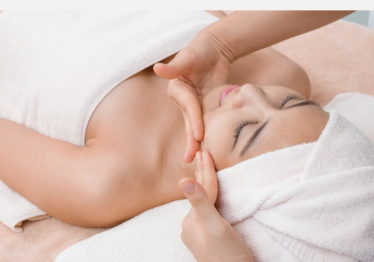 Kvinde får ansigtsmassage med håndklæde om hovedet i spa-miljø.