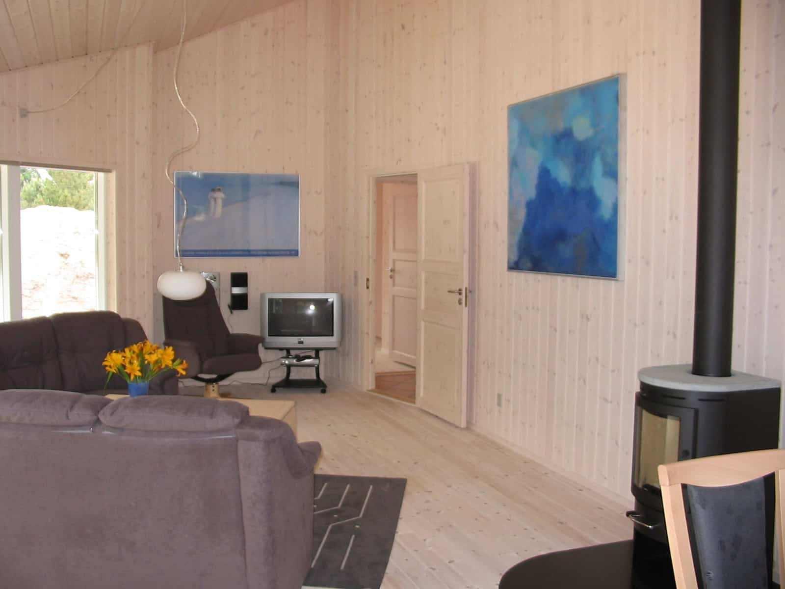 Stue med grå sofaer, tv, malerier på væggene og en brændeovn i et lyst rum med trævægge.